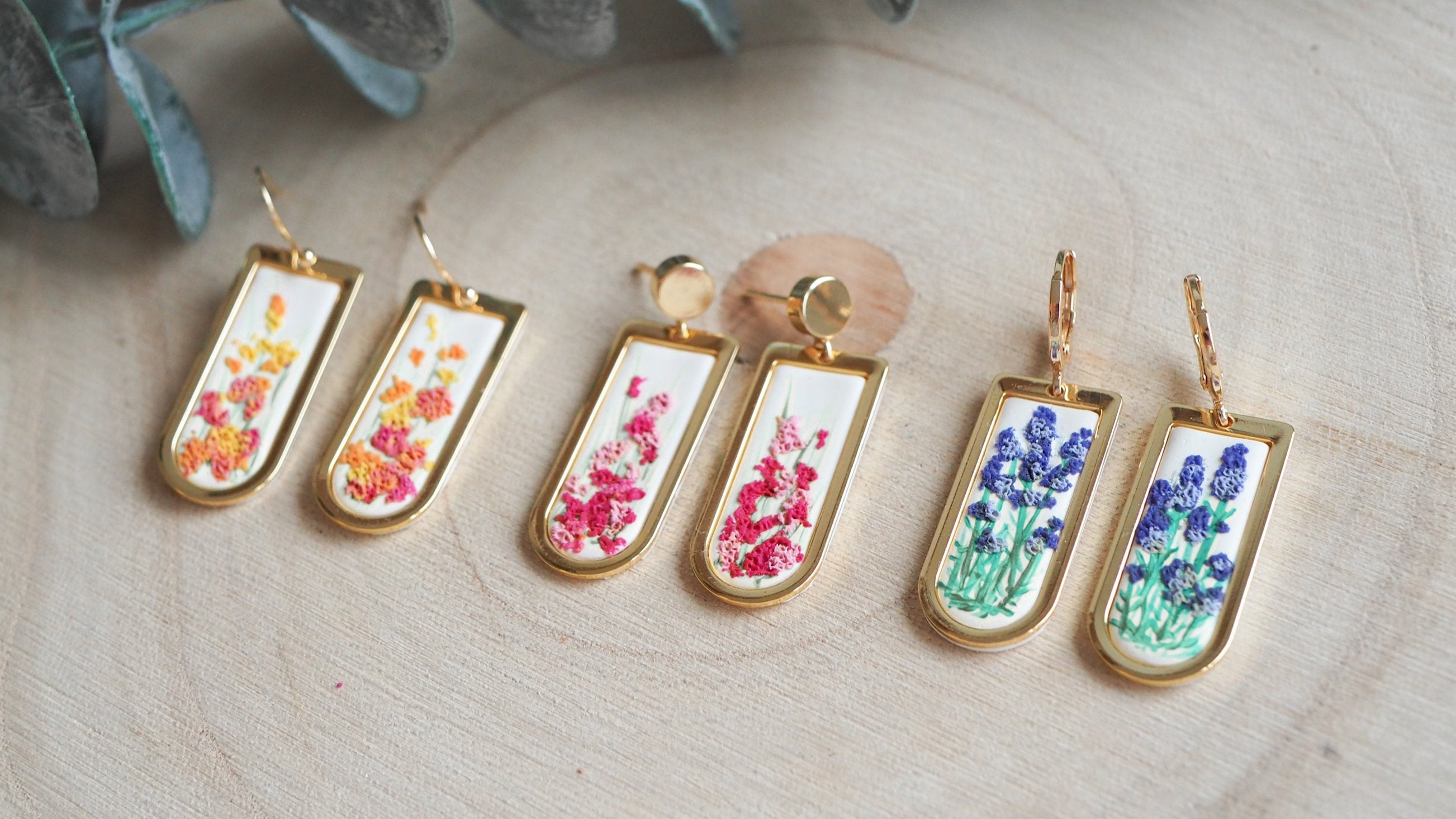 Nahaufnahme von drei Ohrring Paaren aus goldenen Rahmen mit Blumen aus Polymerton.